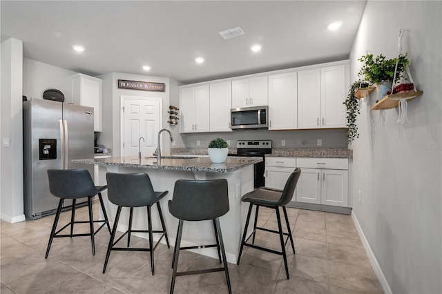 kitchen featuring an island with sink, white cabinetry, a breakfast bar, sink, and appliances with stainless steel finishes