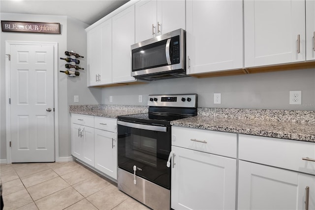 kitchen with white cabinets, light tile patterned flooring, stainless steel appliances, and light stone counters