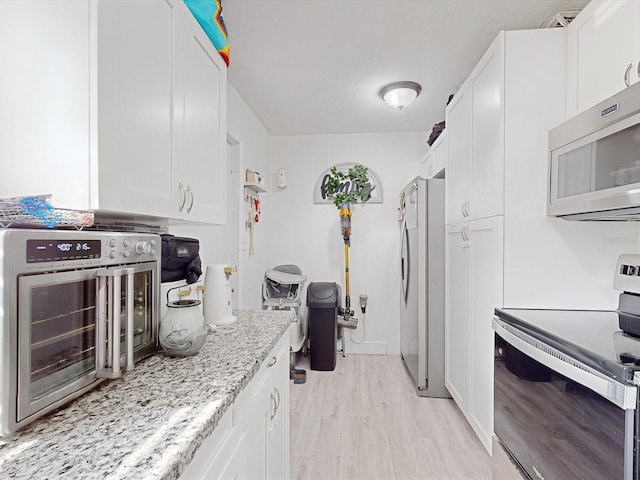 kitchen featuring light stone counters, appliances with stainless steel finishes, light hardwood / wood-style floors, and white cabinets