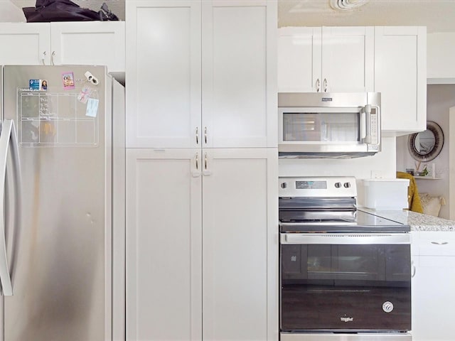 kitchen featuring stainless steel appliances, white cabinets, and light stone counters