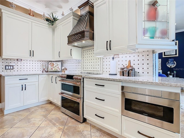 kitchen with premium range hood, white cabinetry, appliances with stainless steel finishes, and tasteful backsplash