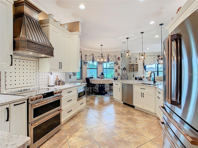 kitchen featuring hanging light fixtures, appliances with stainless steel finishes, custom range hood, and light stone counters