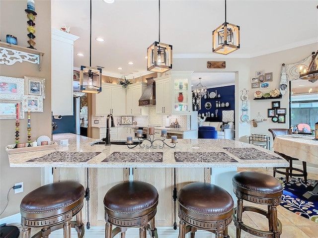 kitchen featuring pendant lighting, sink, white cabinets, a kitchen bar, and wall chimney exhaust hood