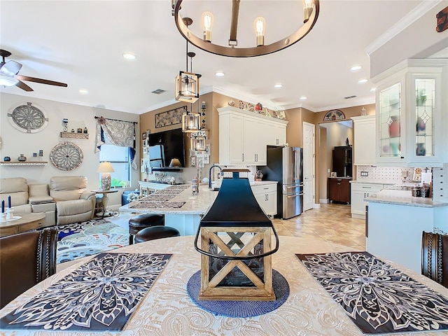 kitchen with a breakfast bar, stainless steel refrigerator, decorative light fixtures, white cabinets, and light stone countertops