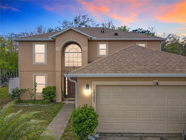 traditional-style home featuring a garage, a shingled roof, and stucco siding