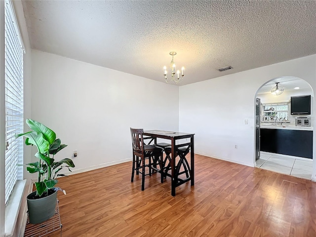 10409 Laxton St, Orlando, FL 32824 - dining room with a chandelier, light wood-style flooring, arched walkways, a textured ceiling, and baseboards