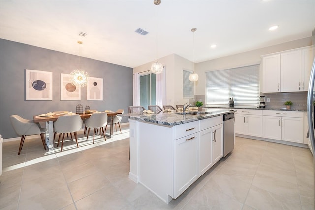 kitchen with pendant lighting, sink, dishwasher, an island with sink, and dark stone counters