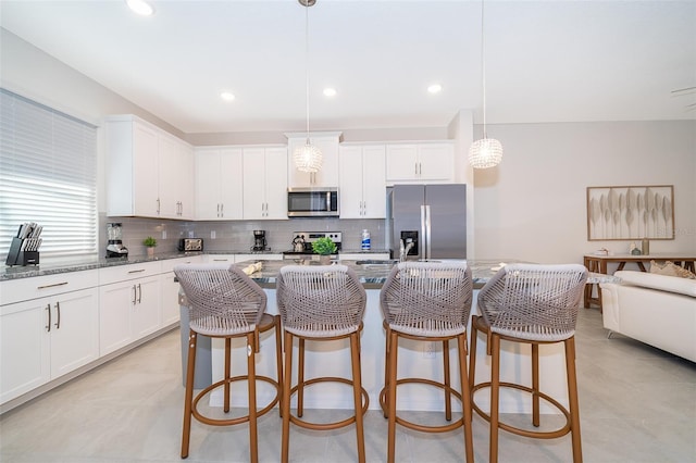 kitchen featuring pendant lighting, appliances with stainless steel finishes, a kitchen island with sink, and dark stone countertops