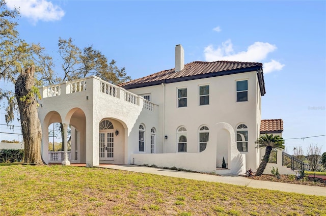 back of property with a lawn, a chimney, a tiled roof, french doors, and stucco siding