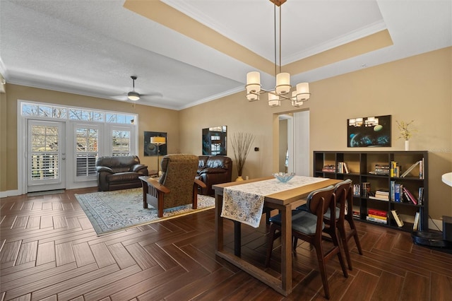 dining area featuring ornamental molding, ceiling fan with notable chandelier, dark parquet flooring, and a raised ceiling