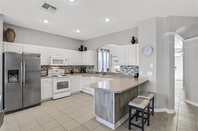 kitchen featuring a breakfast bar, white cabinets, light tile patterned floors, kitchen peninsula, and white appliances