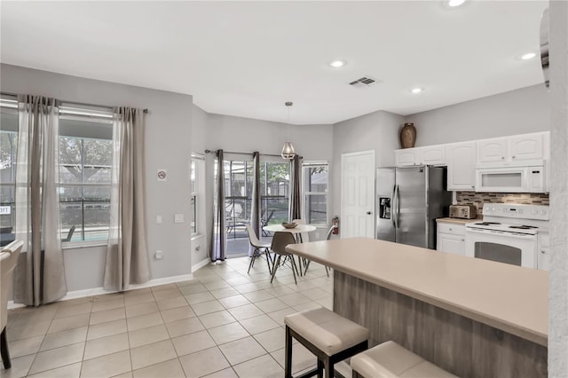 kitchen with light tile patterned flooring, decorative light fixtures, white cabinets, white appliances, and backsplash