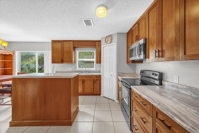 kitchen featuring light tile patterned flooring, black electric range oven, a center island, a textured ceiling, and a kitchen breakfast bar