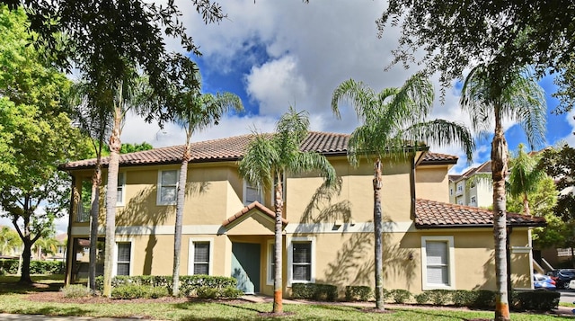 view of front facade with a front yard, a tile roof, and stucco siding