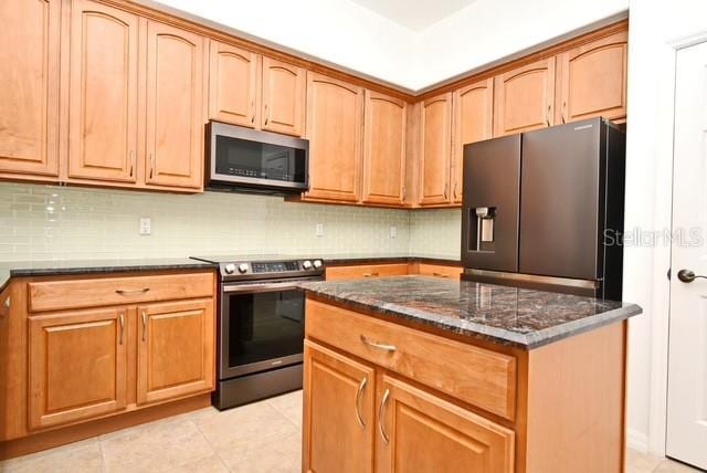 8766 The Esplanade Unit 23, Orlando, FL 32836 - kitchen with light tile patterned floors, decorative backsplash, dark stone counters, a kitchen island, and appliances with stainless steel finishes