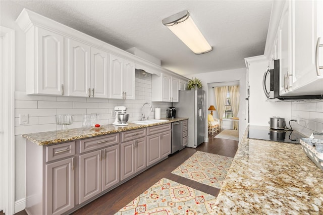 kitchen featuring stainless steel appliances, a sink, white cabinetry, light stone countertops, and dark wood-style floors