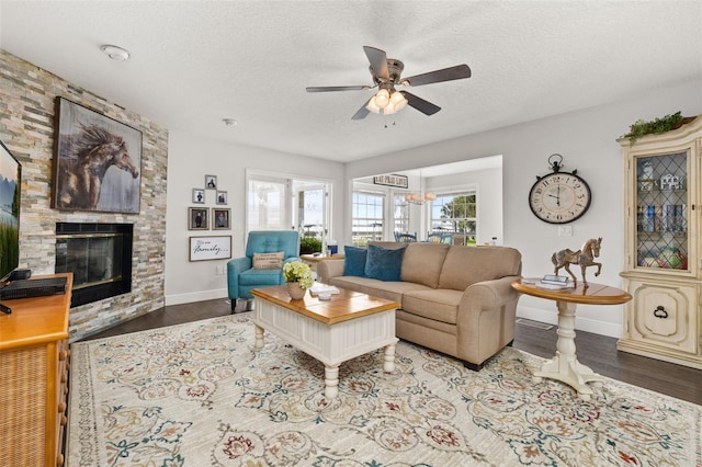 living area with a fireplace, a ceiling fan, a textured ceiling, wood finished floors, and baseboards