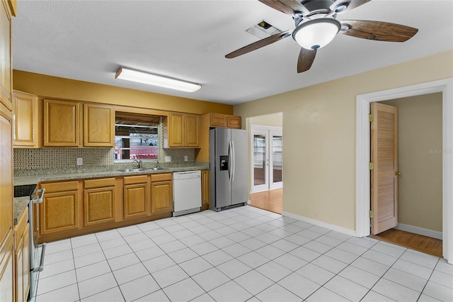 kitchen with light tile patterned flooring, sink, backsplash, ceiling fan, and stainless steel appliances