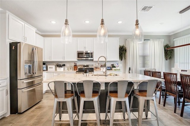 kitchen with appliances with stainless steel finishes, white cabinetry, a kitchen island with sink, and light stone countertops