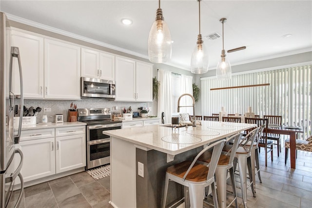 kitchen with hanging light fixtures, a center island with sink, white cabinetry, and stainless steel appliances