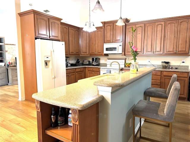 kitchen featuring light hardwood / wood-style flooring, white appliances, an island with sink, decorative light fixtures, and a kitchen bar