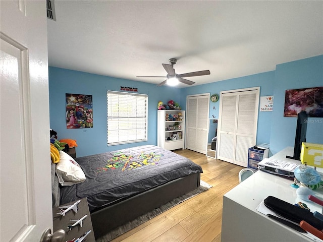 bedroom featuring wood-type flooring, ceiling fan, and multiple closets