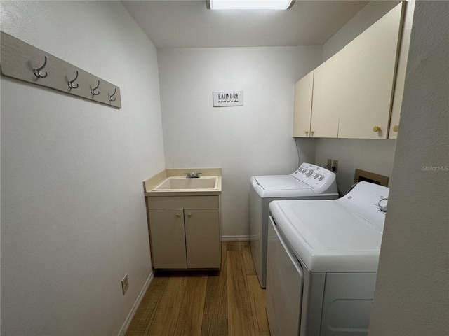 laundry area featuring washing machine and dryer, sink, cabinets, and light hardwood / wood-style floors