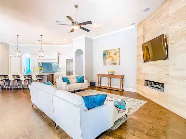 living area featuring crown molding, wood finished floors, ceiling fan, a tile fireplace, and arched walkways
