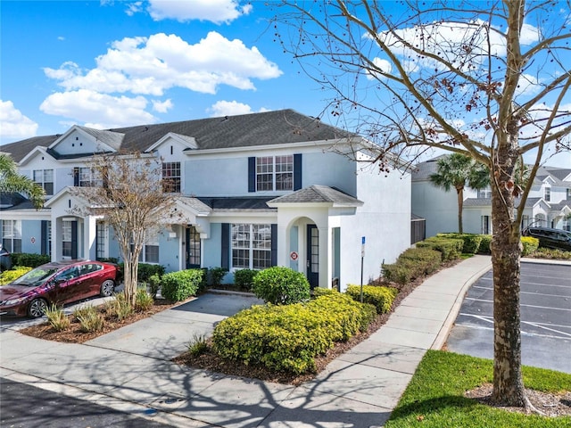 view of front of house featuring uncovered parking, a residential view, a shingled roof, and stucco siding