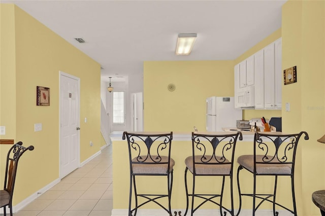 kitchen featuring white appliances, light tile patterned floors, a breakfast bar area, a peninsula, and white cabinetry