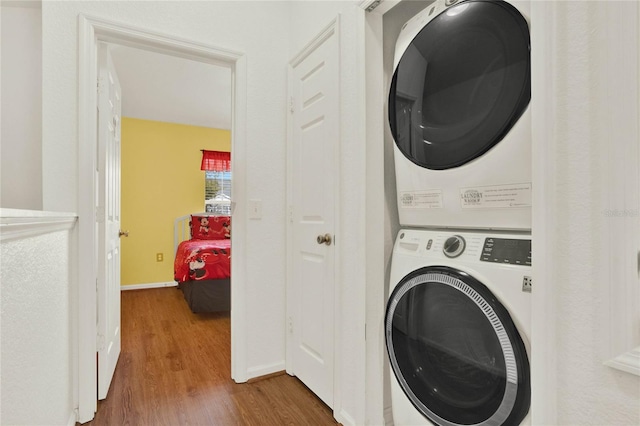 laundry room featuring stacked washer and dryer, baseboards, and wood finished floors