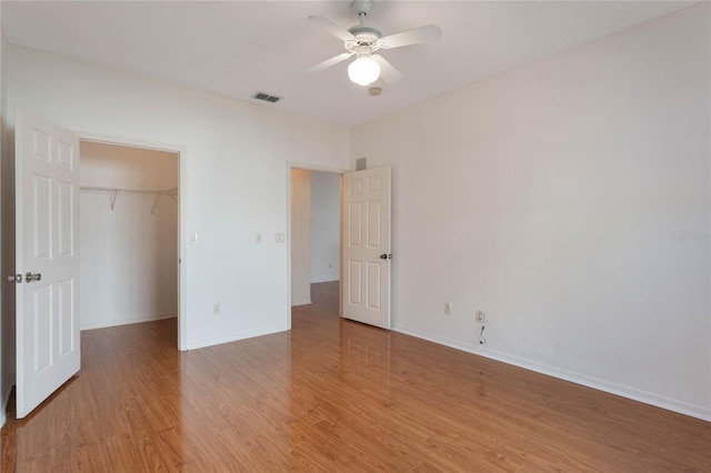 unfurnished bedroom with light wood-type flooring, a closet, ceiling fan, and a spacious closet