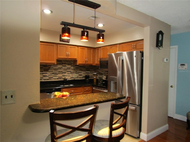 kitchen featuring appliances with stainless steel finishes, dark stone countertops, backsplash, hanging light fixtures, and a kitchen bar