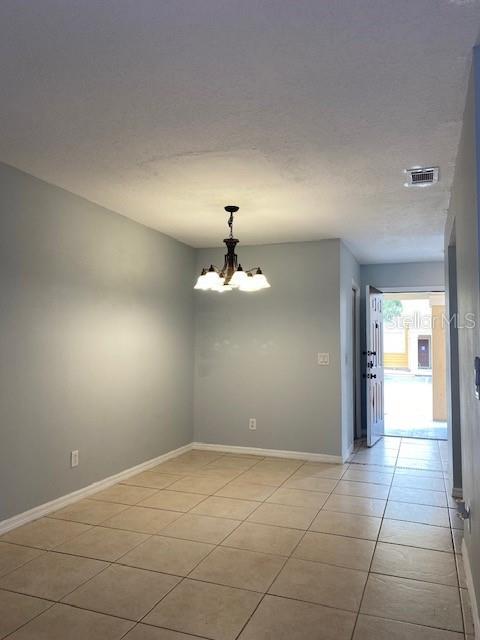 empty room featuring light tile patterned flooring, a textured ceiling, and a notable chandelier