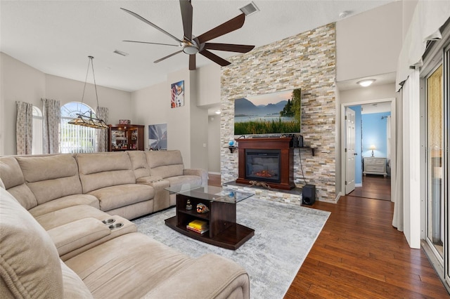 living room featuring ceiling fan, dark wood-type flooring, and a stone fireplace