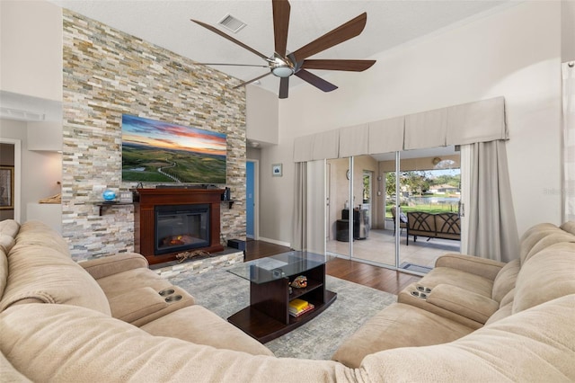 living room featuring light hardwood / wood-style floors, ceiling fan, a towering ceiling, and a fireplace