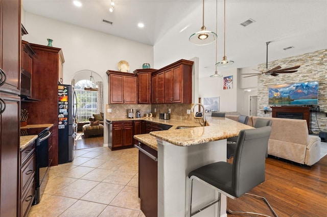 kitchen featuring kitchen peninsula, decorative light fixtures, stainless steel fridge, black electric range oven, and sink