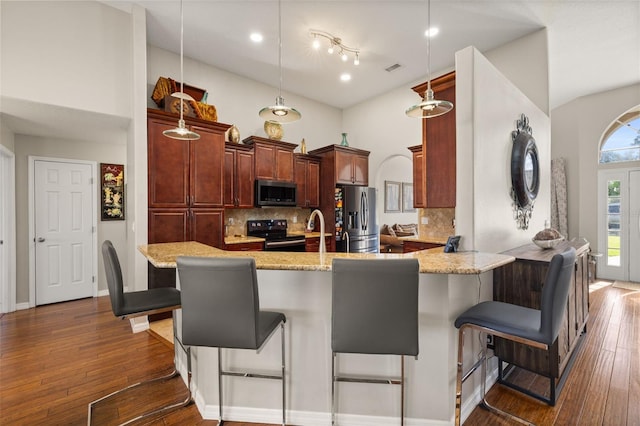 kitchen with a kitchen breakfast bar, kitchen peninsula, decorative light fixtures, appliances with stainless steel finishes, and dark hardwood / wood-style floors