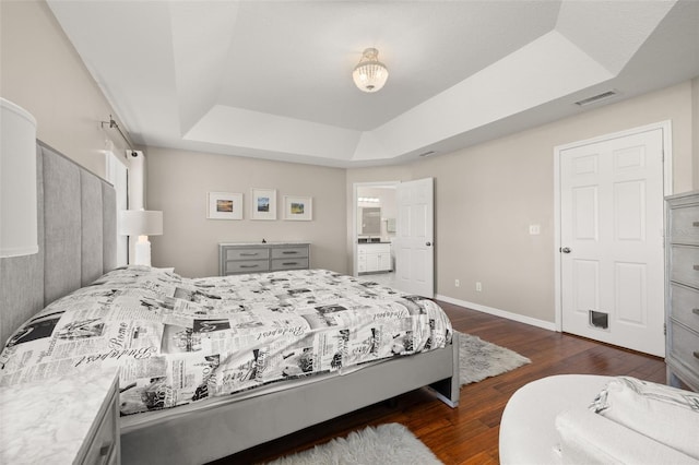 bedroom featuring ensuite bath, a tray ceiling, and dark hardwood / wood-style flooring