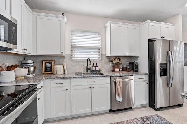 kitchen with tasteful backsplash, stainless steel appliances, a sink, white cabinetry, and light stone counters