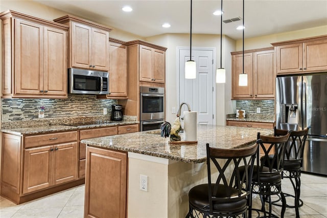 kitchen featuring appliances with stainless steel finishes, a breakfast bar, hanging light fixtures, an island with sink, and light stone countertops