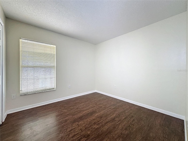 spare room with a textured ceiling, baseboards, and dark wood-type flooring