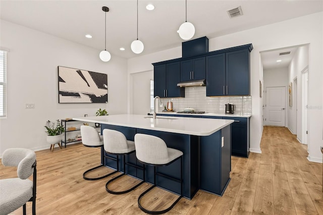 kitchen featuring visible vents, a kitchen island with sink, light countertops, pendant lighting, and a sink