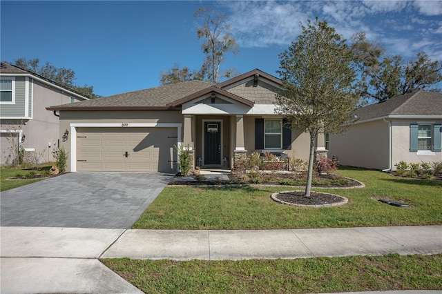 craftsman-style home with a garage, decorative driveway, a front lawn, and stucco siding