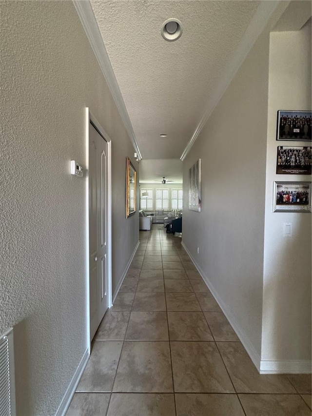 hallway with tile patterned flooring, crown molding, baseboards, a textured wall, and a textured ceiling