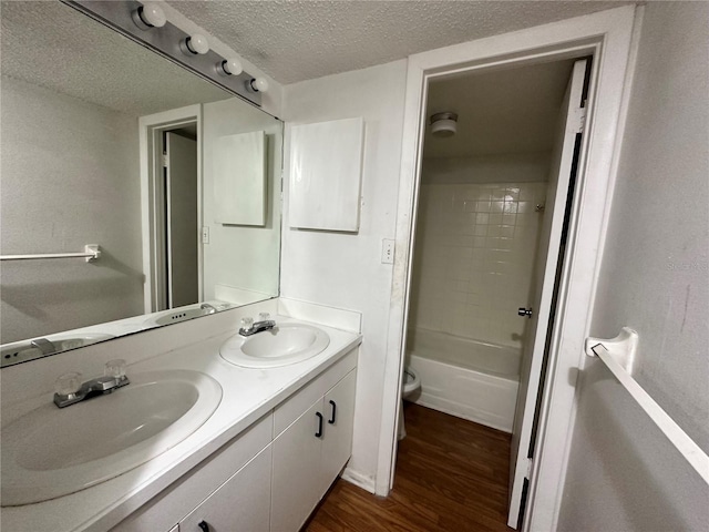 full bathroom featuring double vanity, a sink, a textured ceiling, and wood finished floors