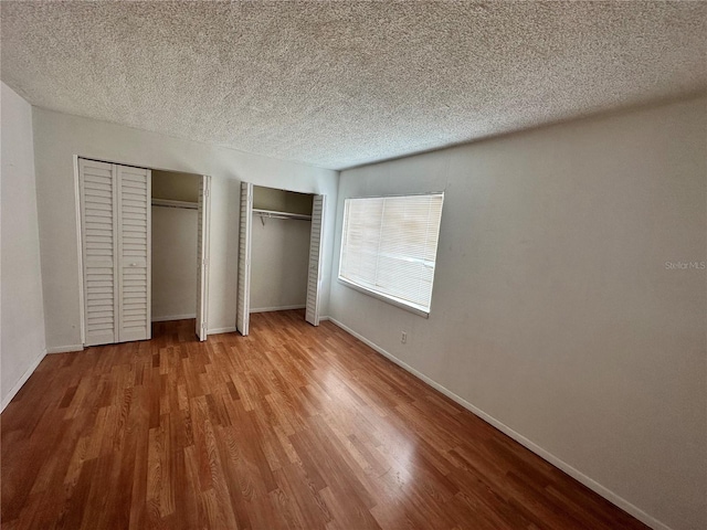 unfurnished bedroom with multiple closets, a textured ceiling, baseboards, and wood finished floors