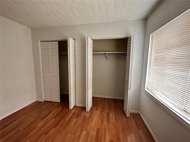 unfurnished bedroom with wood finished floors, a textured ceiling, baseboards, and two closets