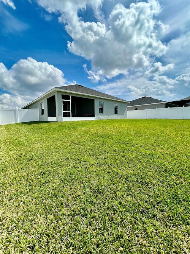 rear view of house featuring a yard, fence, and stucco siding