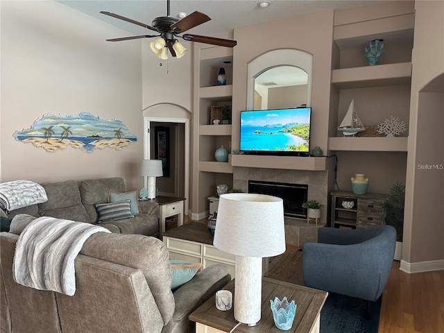 living room featuring hardwood / wood-style flooring, ceiling fan, built in shelves, and a tiled fireplace